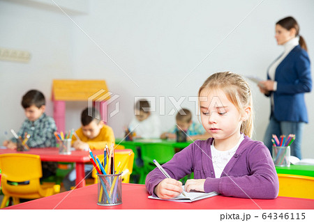 Portrait of little assiduous girl with pen and notebook at lesson in elementary school 64346115