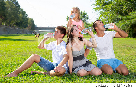 Family sitting on green lawn and drinking water 64347265