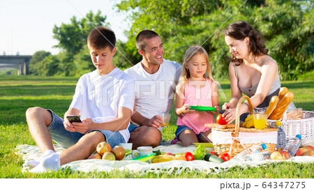 Parents with two teenagers enjoying delicious meal on the picnic 64347275