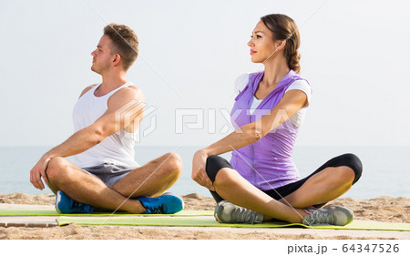 Cross-legged couple practice yoga on beach in morning 64347526