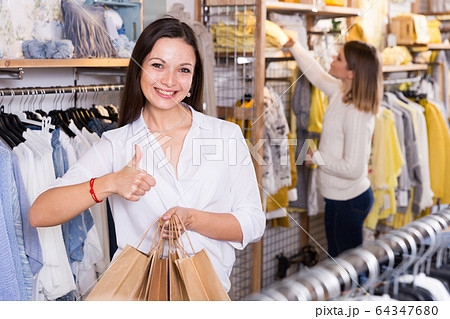 Young woman with paper bags holding thumb up in fashion store Young woman with paper bags holding thumb up in fashion store 64347680