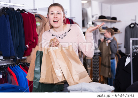 Satisfied girl with purchases in clothes shop 64347843