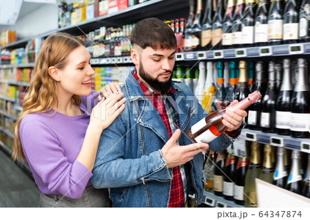 Glad man and woman choosing bottle of cava Glad man and woman choosing bottle of cava 64347874