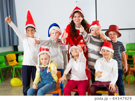 Pupils with teacher in Santa hats giving thumbs up 64347929