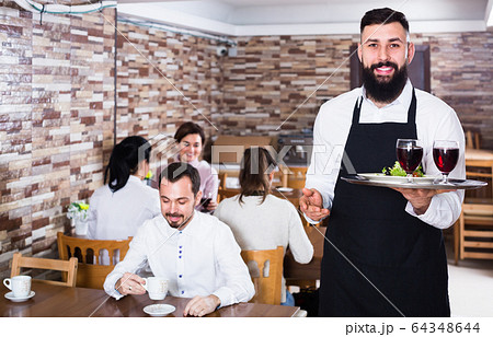 Smiling waiter taking care of adults at cafe table Smiling waiter taking care of adults at cafe table 64348644