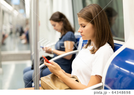 Woman sitting in subway car with phone Woman sitting in subway car with phone 64348698