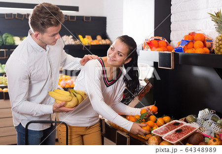 Positive couple deciding on fruits in shop Positive couple deciding on fruits in shop 64348989