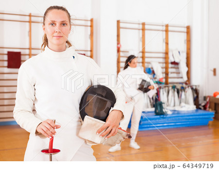 Smiling young female in uniform standing at fencing room 64349719