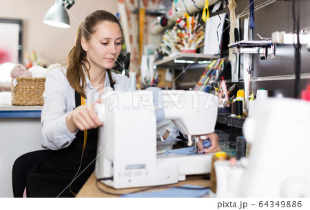 Female tailor working with sewing machine at workshop Female tailor working with sewing machine at workshop 64349886