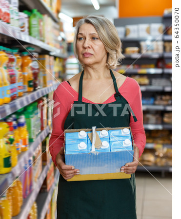 Adult saleswoman in apron arranging products Adult saleswoman in apron arranging products 64350070