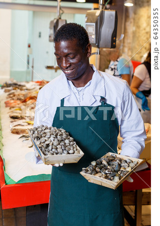 Salesman offering fresh clams in fish store 64350355
