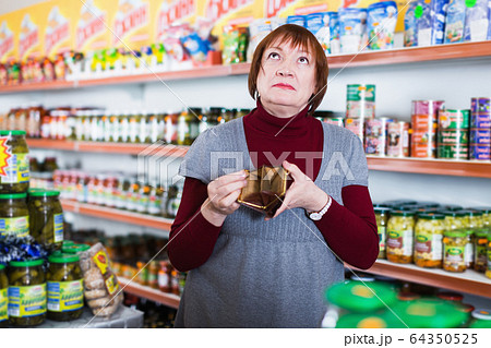 Sad mature woman buyer with empty purse and canned 64350525