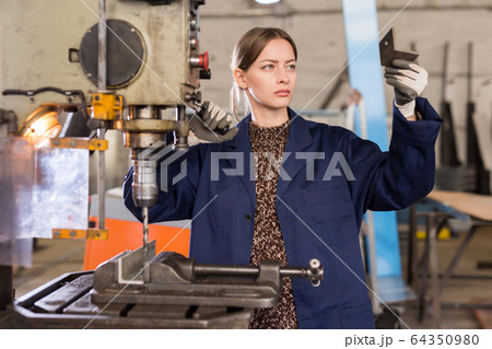Portrait of female working with drilling machine on metal plate Portrait of female working with drilling machine on metal plate 64350980