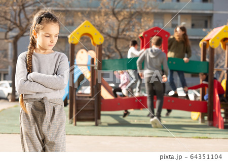 Upset little girl standing on playground 64351104