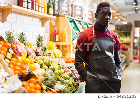 Seller of fruits and vegetables store standing with crossed arms 64351205