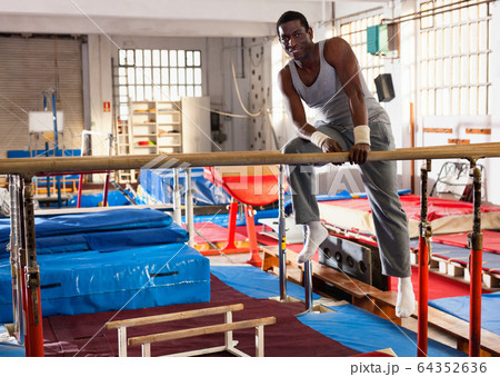 Portrait of man in sportswear doing exercises on parallel bars at gymnastic hall 64352636