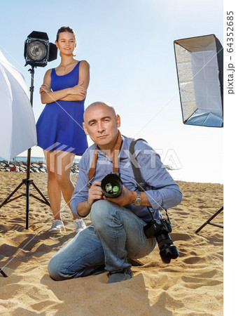 Portrait of male photographer with camera among professional photo equipment on seaside 64352685