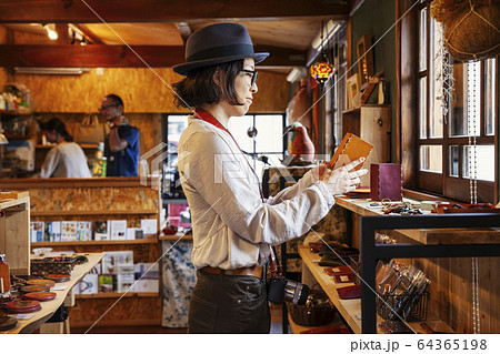 Japanese woman wearing hat and glasses browsing merchandise in a leather shop. Japanese woman wearing hat and glasses browsing merchandise in a leather shop. 64365198