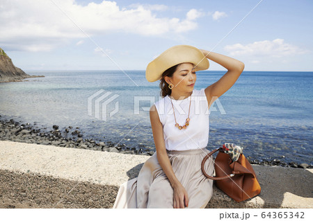 Japanese woman wearing hat sitting on a wall, ocean in the background. Japanese woman wearing hat sitting on a wall, ocean in the background. 64365342
