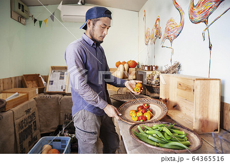 Japanese man wearing cap standing in farm shop, holding bowl with fresh vegetables. Japanese man wearing cap standing in farm shop, holding bowl with fresh vegetables. 64365516