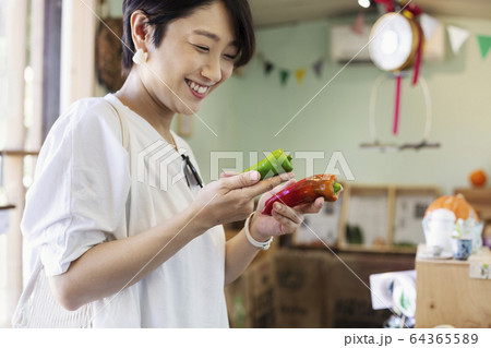 Smiling Japanese woman standing in a farm shop, holding vegetables. 64365589