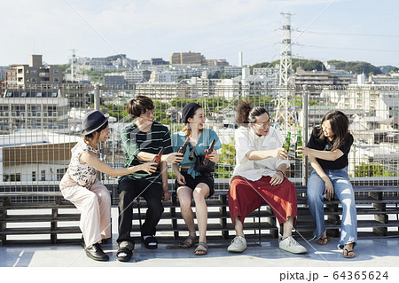 Group of young Japanese men and women sitting on a rooftop in an urban setting, drinking beer. 64365624