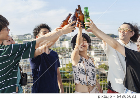 Group of young Japanese men and women standing on a rooftop in an urban setting, drinking beer. 64365633