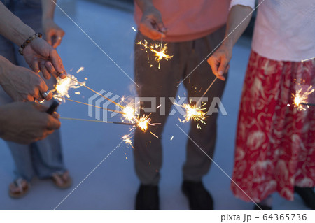 Group of young men and women with sparklers on a rooftop in an urban setting. Group of young men and women with sparklers on a rooftop in an urban setting. 64365736