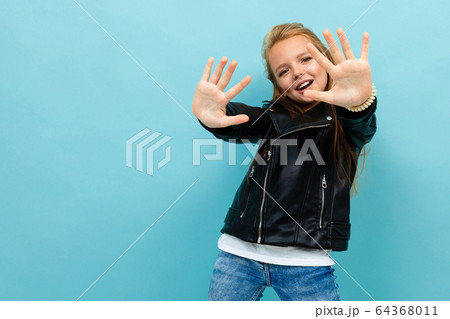 cute girl in a casual look with a leather jacket and jeans pulls his hands forward against a light cute girl in a casual look with a leather jacket and jeans pulls his hands forward against a light 64368011