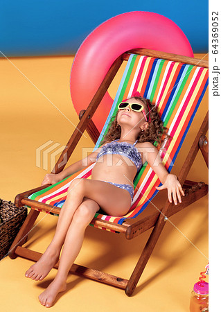 Girl in swimsuit and sunglasses lying in rainbow deck chair with crossed legs and sunbathing Girl in swimsuit and sunglasses lying in rainbow deck chair with crossed legs and sunbathing 64369052