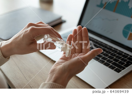 Female employee cleanse hands with sanitizer at workplace Female employee cleanse hands with sanitizer at workplace 64369439