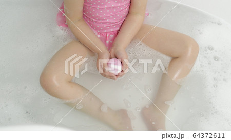 Hands of girl puts bath bomb to water. Ball of bath salt dissolves in water Hands of girl puts bath bomb to water. Ball of bath salt dissolves in water 64372611