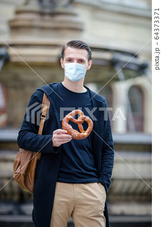 Beautiful young man holding pretzel and relaxing in park Beautiful young man holding pretzel and relaxing in park 64373371