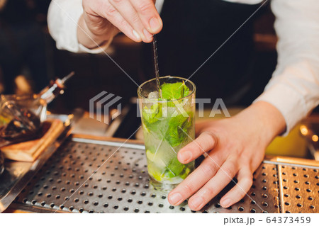 Barman makes a cocktail on the bar in the restaurant. 64373459
