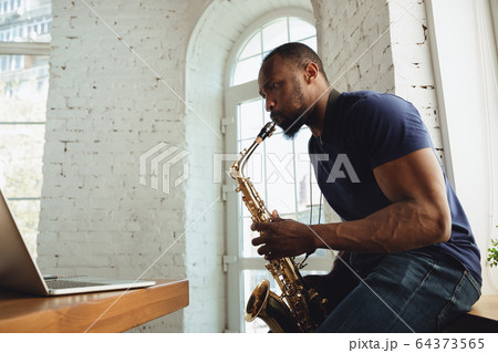 African-american musician playing saxophone during online concert at home isolated and quarantined, impressive improvising 64373565