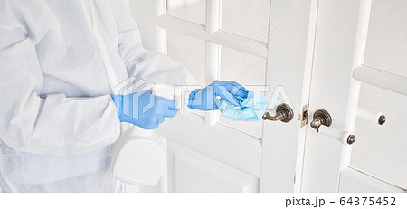 Disinfection, cleaning and washing of door handles. COVID-19. Prevention of coronavirus infection. A woman in a protective suit and blue gloves sprays a disinfectant solution. 64375452