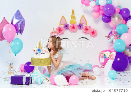 Unicorn Girl posing near happy birthday cake. Idea for decorating unicorn style birthday party. Unicorn decoration for festival party girl 64377710