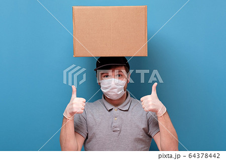Smiling young delivery man in medical mask holding Smiling young delivery man in medical mask holding 64378442