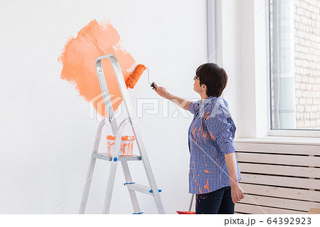 Renovation, redecoration and repair concept - middle-aged woman painting wall in new home. 64392923