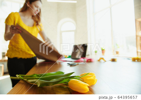 Florist at work: woman shows how to make bouquet with tulips, working at home concept, using coverage paper 64395657