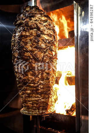 Charcoal shawarma meat. Closeup of chicken meat collected on a vertical skewer and grilled on charcoal. 64396287