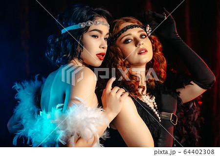 Portrait of young flapper women dressed in style of Great Gatsby posing on dark velours background Portrait of young flapper women dressed in style of Great Gatsby posing on dark velours background 64402308