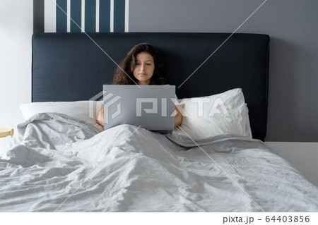 Beautiful brunette girl in bed with a laptop. Work 64403856