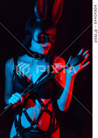 sexy girl mistress in leather harness and Bunny mask holds a Flogger whip 64404904