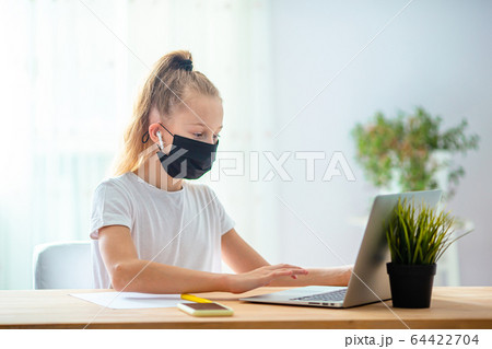 Serious schoolgirl sitting at table with laptop and textbook and doing homework. 64422704