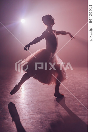 Ballet dancer in tutu performing, jumping on stage. Ballerina practices on floor in dark studio with 64429911