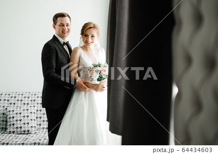 Beautiful young wedding couple posing with bouquet of flowers in hands Beautiful young wedding couple posing with bouquet of flowers in hands 64434603