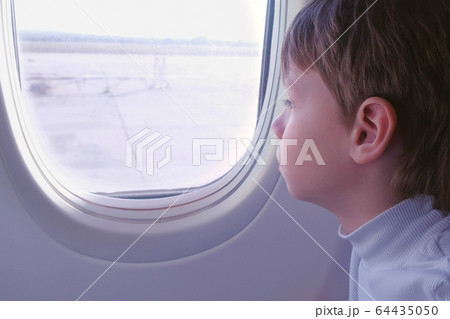 Boy looks out the window when the plane takes off. Side view. Boy looks out the window when the plane takes off. Side view. 64435050
