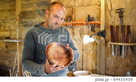 Carpenter in sawdust inspects finished product. 64435439
