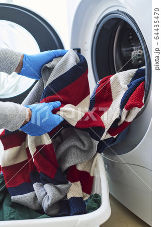 man putting clothes into the washing machine 64435470